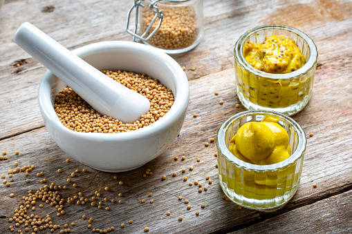Bowl of mustard seeds and different types of mustard on a rustic wooden board