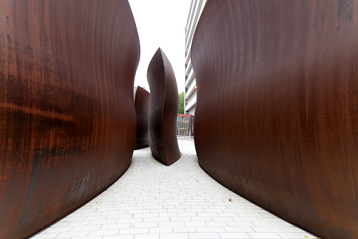 Red brown rusty iron sculpture with walking woman at Novartis Campus at City of Basel on a gray autumn day morning. Photo taken October 3rd, 2022, Basel, Switzerland.