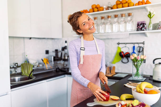 istock Young woman at home in the kitchen preparing a fruit salad looking at camera 1451788714