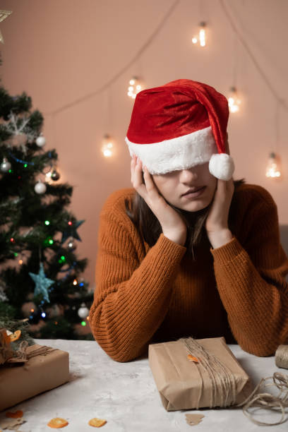 istock tired young woman in a New Year's hat pulled over her eyes taking an order for gift wrapping, in the background a Christmas tree and lights, the concept of preparing for the new year, merry christmas, new year 2023 1451791847