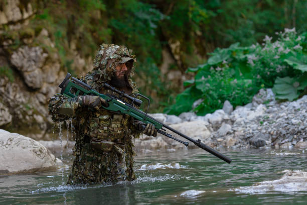 迷彩服を着た軍人またはエアガン奏者が川をこっそりと歩き回り、スナイパーライフルから横または標的を狙う。 - wet spy men suit ストックフォトと画像