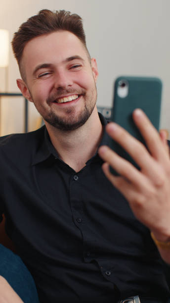 istock Young bearded man making smartphone call conversation online with friends sitting on couch at home 1451804906