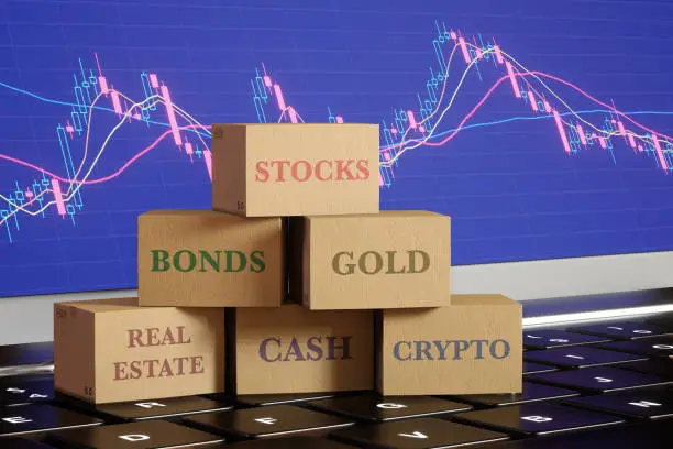 Photo of Carton boxes labelled as different investment product categories on a laptop showing stock candle diagram. Illustration of well-diversified portfolios and the importance of asset diversification.