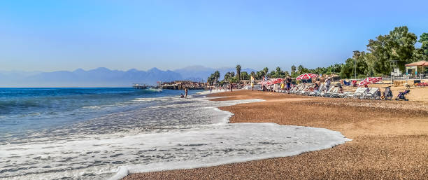 Antalya, Turkey - October 26, 2019: Wide view sea panorama on Lara beach in Antalya. White sea foam washes the sand against the backdrop of people resting on the shores of the Mediterranean Sea