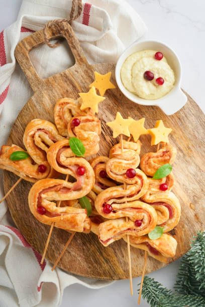 istock Christmas or New Year appetizer. Christmas tree shape puff pastry buns with cheese and ham. Group of Christmas tree shapes on wooden board. Festive idea for Christmas or New Year dinner. Top view. 1451810260