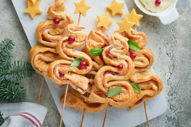 istock Christmas or New Year appetizer. Christmas tree shape puff pastry buns with cheese and ham. Group of Christmas tree shapes on marble stand. Festive idea for Christmas or New Year dinner. Top view. 1451810281
