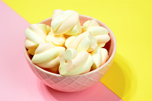 pink bowl with apricot marshmallows isolated on pink and yellow background, macro
