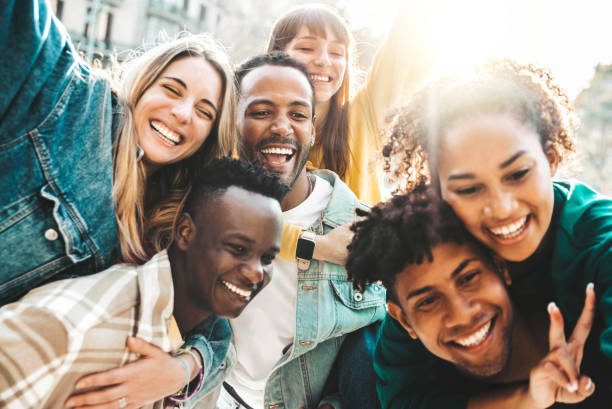 Happy multiracial friends having fun hanging out on city street - Group of young people laughing out loud together outside - Friendship concept with guys and girls enjoying weekend stock photo