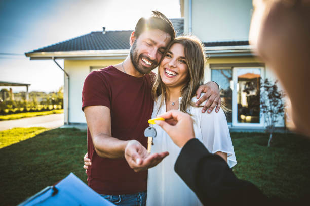 Happy millennial couple receiving keys from Real Estate Agent, purchasing real estate - Family meeting with real estate agent - New house and real estate concept stock photo