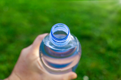 First person point of view of plastic bottle of mineral water that is put in the mouth to drink. Selective focus on the spout of the plastic bottle and defocused natural background and copy space.