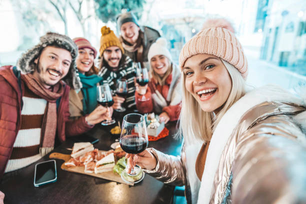 Happy friends celebrating Christmas and new year eve party together - Cheerful young people holding wine glasses taking selfie picture sitting at bar restaurant - Beverage and winter holiday concept stock photo