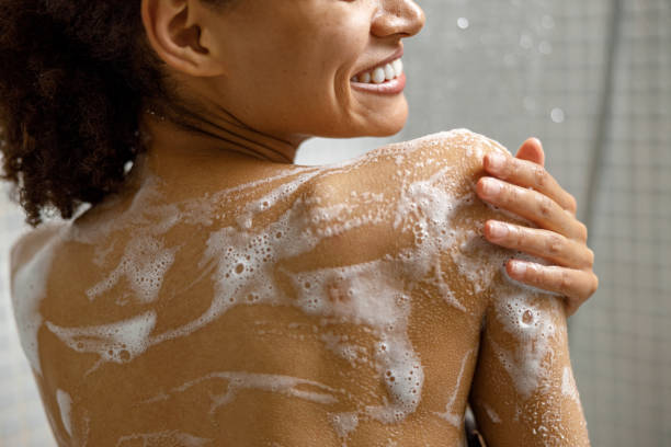 gros plan d’une femme africaine souriante prenant une douche avec du gel ou de la mousse de shampooing dans la salle de bain - savon photos et images de collection