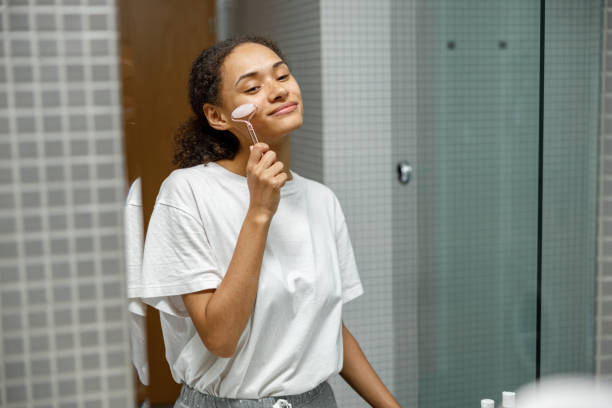 istock Woman making face massage using face roller with quartz stone in bathroom. Natural cosmetics concept 1451833028