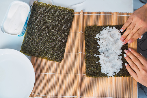 Above image of unrecognizable woman's hands preparing homemade sushi at his kitchen table.