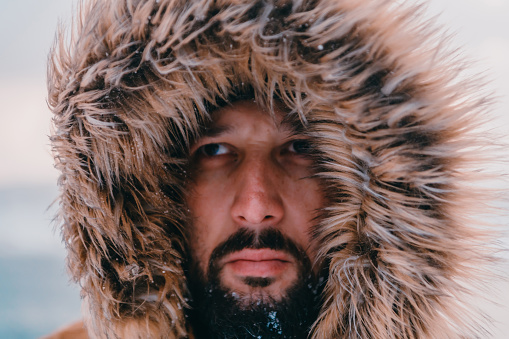 Headshot photo of a man in a cold snowy area wearing a thick brown winter jacket and gloves. Life in cold regions of the country