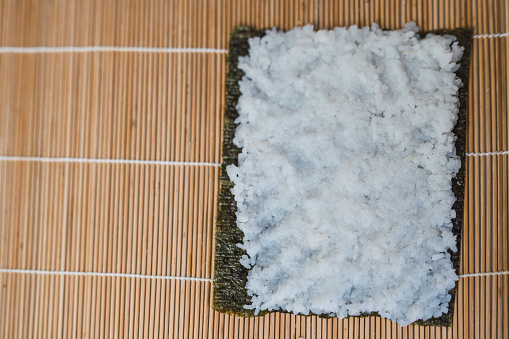 Image above of a rolling mat with a sheet of nori seaweed filled with white rice ready to make homemade sushi.