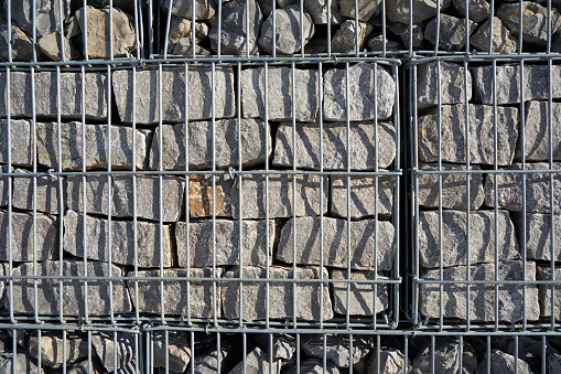 Gabion fence made of steel bars filled with gray granite stone. Full frame. Front view.