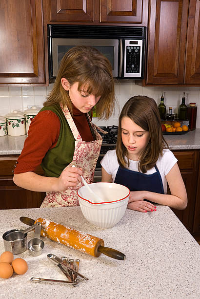 Teenager Teaching Younger Girl to Bake stock photo