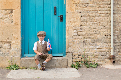 A boy is dressed up in vintage and retro clothing on a local street in England celebrating his heritage. Image taken in the Cotswolds, England.