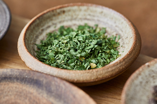 Parsley in a ceramic bowl on a kitchen table, on a kitchen cutting board, on an oak wooden table top, a macro photo shoot texture background, image with a copy space