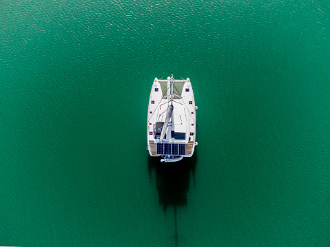 Aerial view of a sailing catamaran with solar frame in green waters