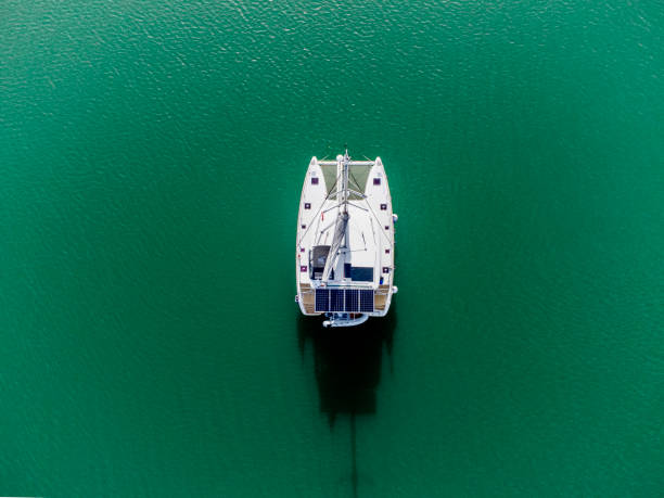 Sailing catamaran in green waters Aerial view of a sailing catamaran with solar frame in green waters catamaran sailing stock pictures, royalty-free photos & images