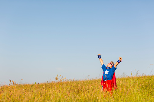 A young boy is dressed as a superhero standing on a grassy hill. He is ready to show his new powers and confidence to the world. Image taken in Wiltshire, UK.
