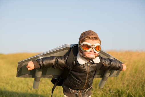 A young boy pilot dressed in bomber jacket, flying goggles, and flying cap is wearing a homemade jetpack. He is ready to test his new invention and take his game to the skies. Image taken in Wiltshire, UK.