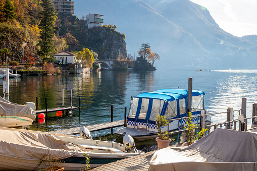 Sheltered boats in the foreground and kayaks in the background: training or competition in good autumn or winter day  on Lugano lake! And awe autumn leaf color!
