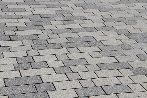 Stock photo showing an elevated view of a herringbone patterned driveway being constructed with grey, rectangular blocks, with brick edging where the drive meets the tarmac pavement.