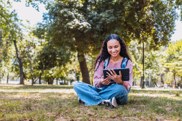 istock Black university student woman smiling and using a tablet sitting outside in a park on the grass 1451848941