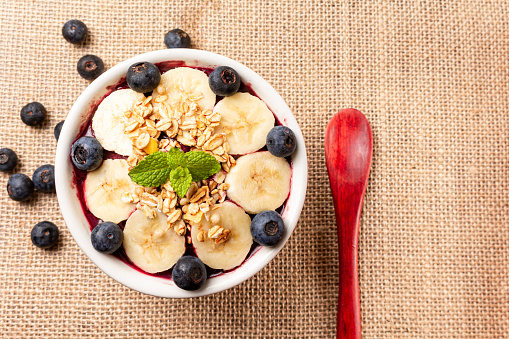 Acai bowl with berries and cereal and spoon on the side, on jute surface. Brazilian popular dessert.