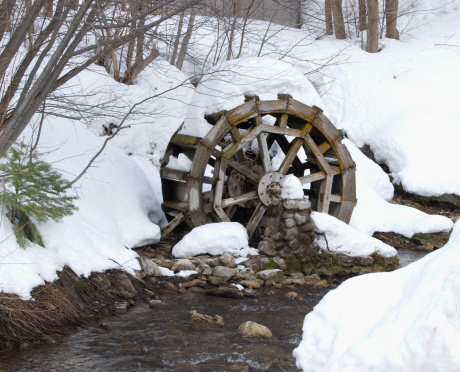 Water wheel covered by snow next to a stream.