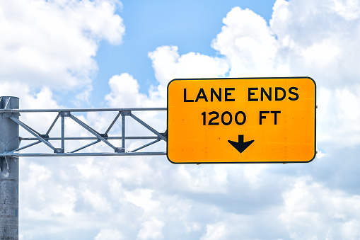Closeup of lane ends in 1200 feet highway road above sign isolated against blue sky clouds in Florida