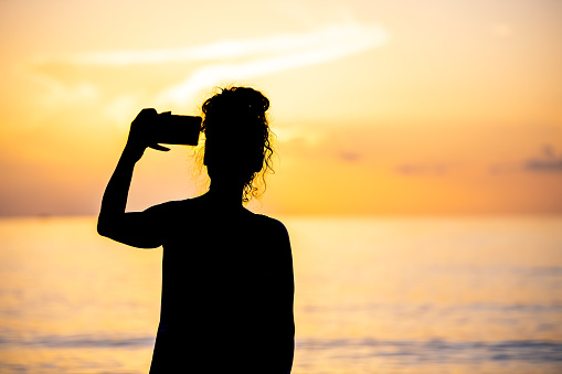 Hollywood Beach in Miami, Florida morning sunrise or sunset with reflection path, woman taking photo selfie picture photographing with phone camera