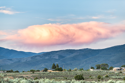 Panoramic view of sunset by desert sage brush plants in Ranchos de Taos valley, New Mexico with Sangre de Cristo mountains summer clouds landscape