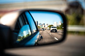 Car window side mirror on sunny day with truck traffic in reflection in Richmond, Virginia transportation highway street road