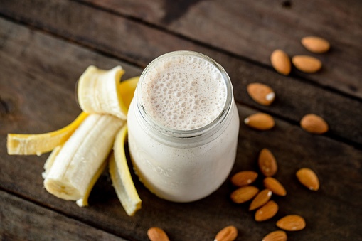 A top view shot of a banana protein shake with a half banana and almond nuts on the table