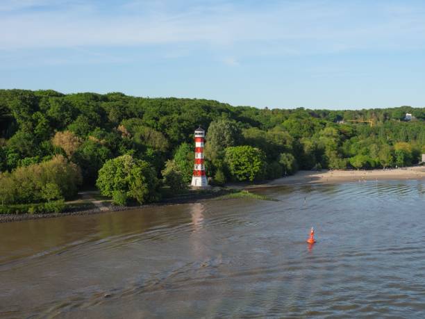 A lighthouse on the Elbe riverbank with dense trees in Hamburg, Germany