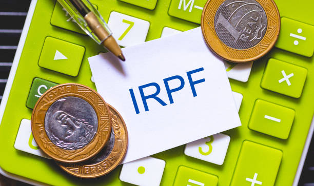 инициалы irpf написаны синим цветом на небольшом листе бумаги. ручка и калькулятор в композиции. бразильская экономика, подоходный налог. - text pen letter metal стоковые фото и изображения