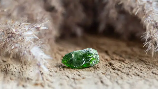 Green Raw Chrome Diopside or Siberian Emerald Mineral Stone on Natural Wooden Background.