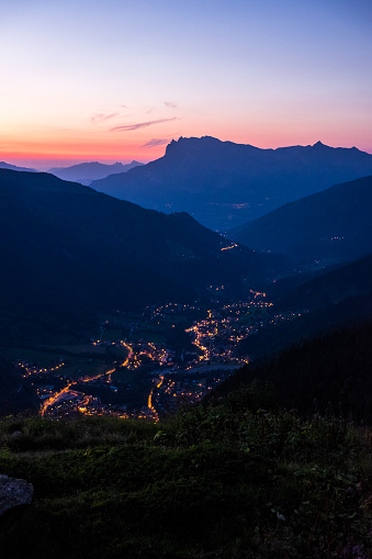A gorgeous vertical shot of a mountain range with city lights in the middle during an orange sunset