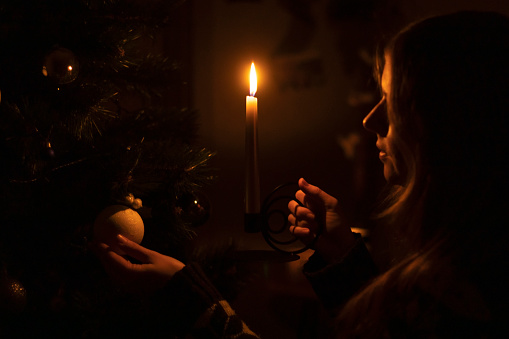 Ukraine, winter 2022. A woman decorates a Christmas tree in the dark with a candle.