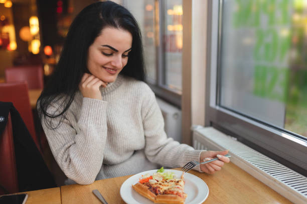 istock Beautiful young woman eating pizza in a restaurant 1451885605