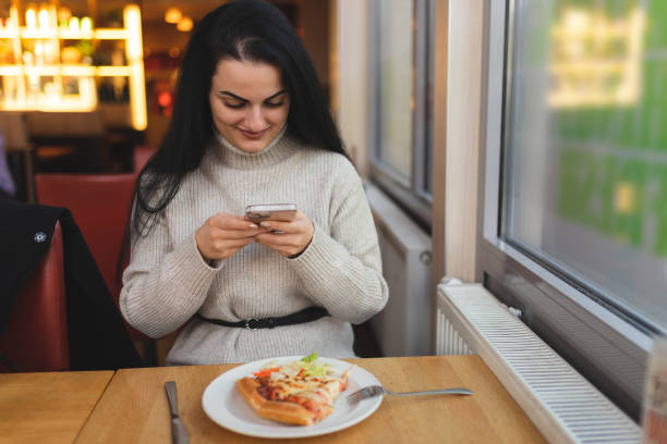 istock Beautiful young woman using her phone while having lunch in a restaurant 1451885677