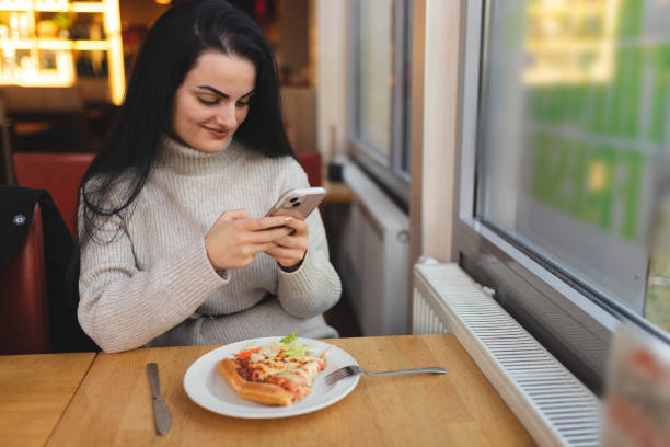 istock Beautiful young woman using her phone while having lunch in a restaurant 1451885703