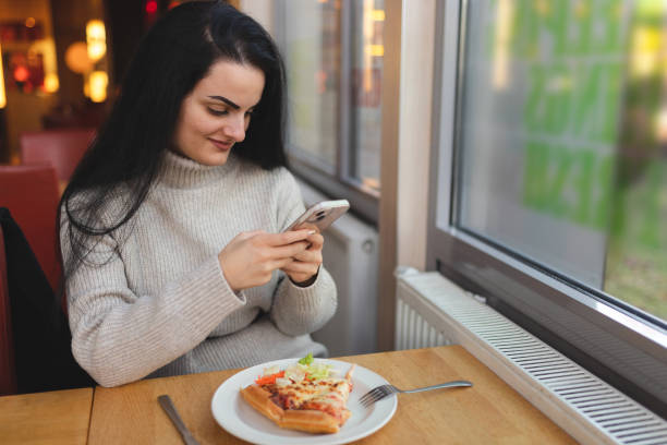 istock Beautiful young woman using her phone while having lunch in a restaurant 1451885716
