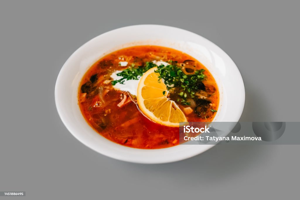hodgepodge soup with lemon in a white plate. hodgepodge soup with slice of lemon in a white plate on gray solid background. Front view. Appetizer Stock Photo