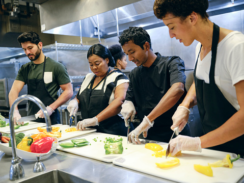 A teaching chef works with a group of students in a commercial kitchen.