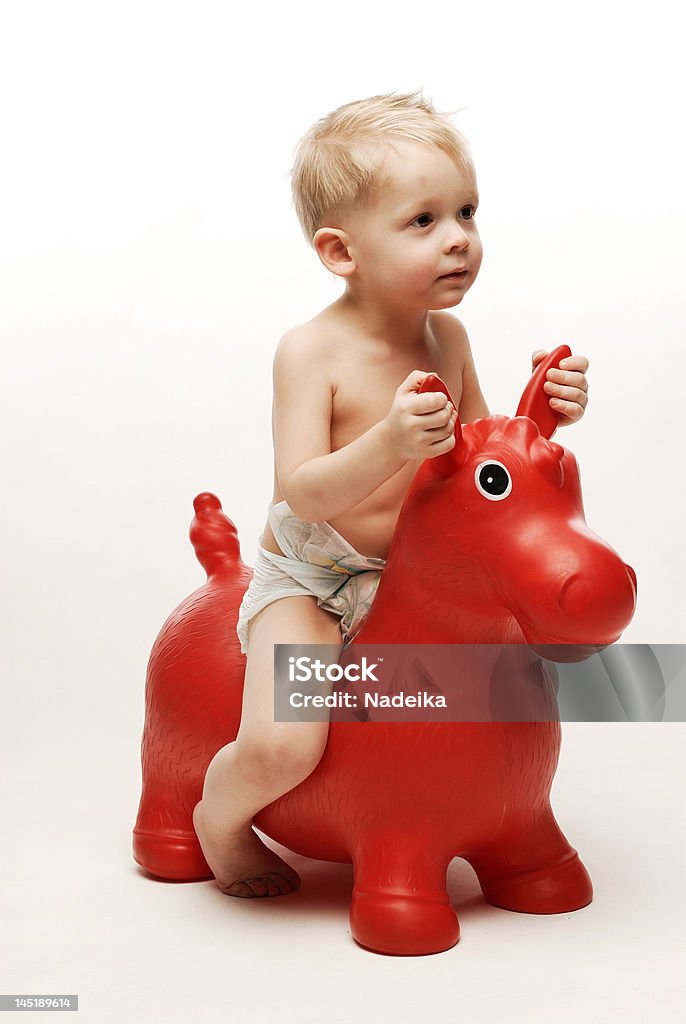Mały chłopiec siedzi na czerwone konia trzymając ją za uszy - Zbiór zdjęć royalty-free (Jeździć)
